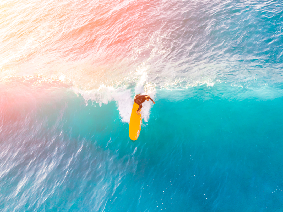 Surfer mit gelbem Surfbrett auf einer großen Welle im Sonnenlicht, Symbol für Balance und emotionale Stärke.