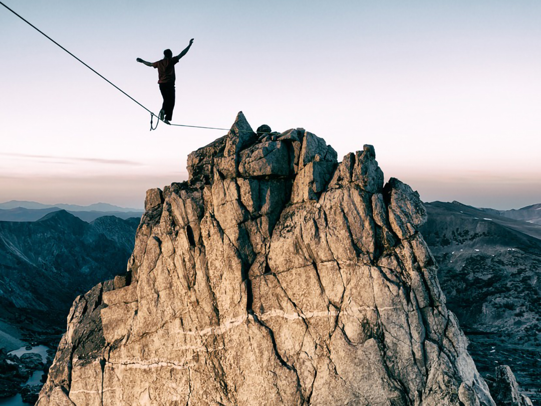 Person balanciert auf einem Seil über einem Felsgipfel bei Sonnenuntergang – symbolisch für emotionale Balance und Resilienz im 1:1 Coaching.